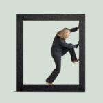 A businesswoman attempts to free herself from the parameters established around her as she lifts her leg to help push against the boundaries.