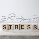 6 small wooden cubes with the word Stress written on them. Speech bubbles above them with the words: busy, overload, chaos, pressure, anxiety